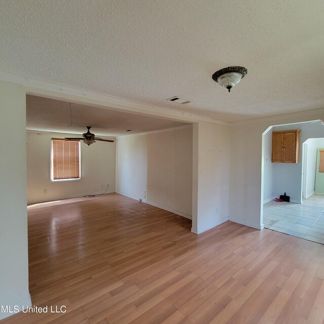 empty room featuring crown molding, a textured ceiling, arched walkways, and light wood-type flooring