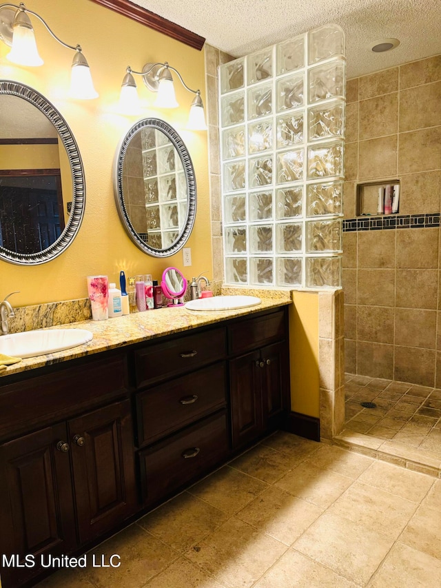 bathroom with a tile shower, a textured ceiling, tile patterned floors, vanity, and crown molding