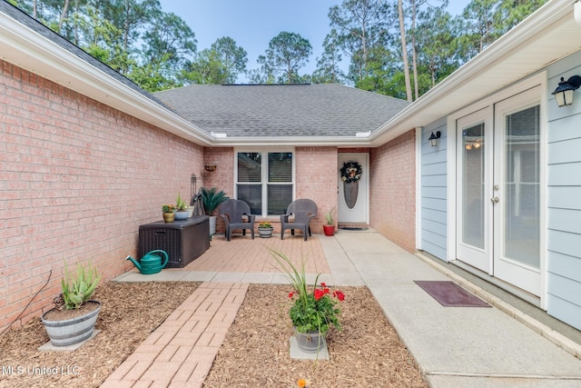 doorway to property featuring roof with shingles, a patio, french doors, and brick siding
