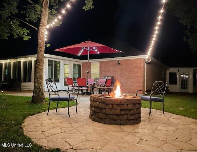back of house at night featuring an outdoor fire pit, a patio area, and brick siding