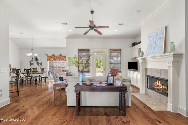 living room featuring ornamental molding, ceiling fan with notable chandelier, wood-type flooring, and a tile fireplace