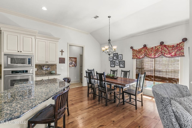 dining area featuring crown molding, a notable chandelier, wood-type flooring, and lofted ceiling