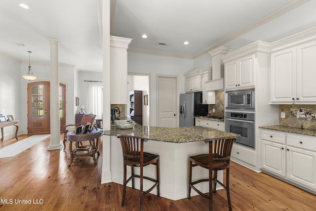 kitchen featuring white cabinets, stainless steel appliances, ornate columns, and light wood-type flooring