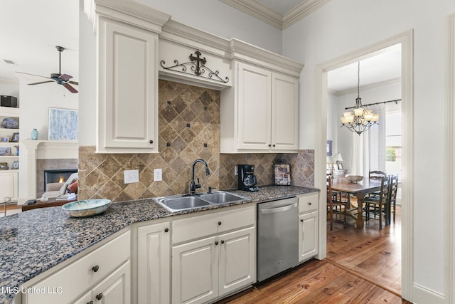 kitchen with white cabinetry, wood-type flooring, dishwasher, a tile fireplace, and sink