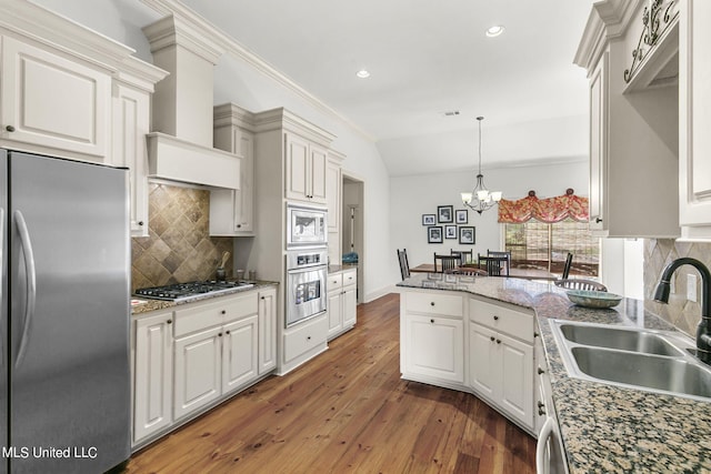 kitchen featuring dark wood-type flooring, sink, vaulted ceiling, decorative light fixtures, and appliances with stainless steel finishes