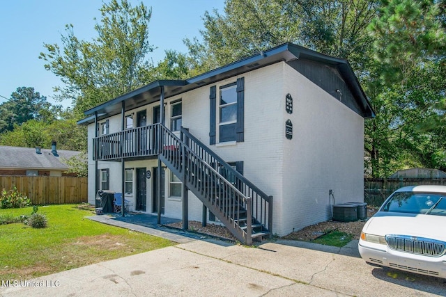 view of property with a front lawn, fence, stairway, cooling unit, and brick siding