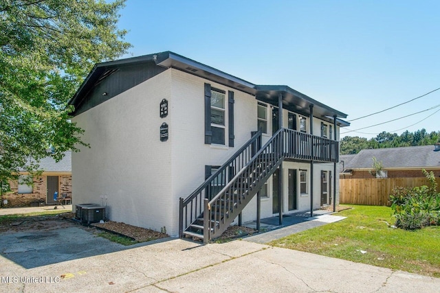 view of front of home with brick siding, a front lawn, fence, stairway, and central AC