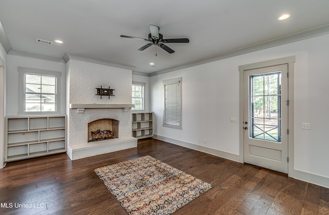 unfurnished living room with a brick fireplace, dark wood-type flooring, ornamental molding, and ceiling fan