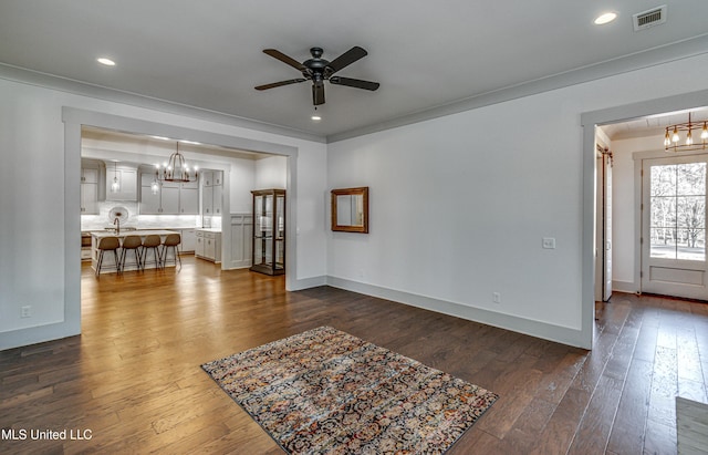 unfurnished living room with ceiling fan with notable chandelier, dark wood-type flooring, and ornamental molding