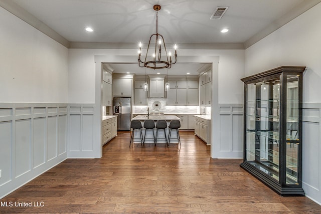 kitchen with stainless steel fridge with ice dispenser, an inviting chandelier, an island with sink, decorative light fixtures, and a breakfast bar