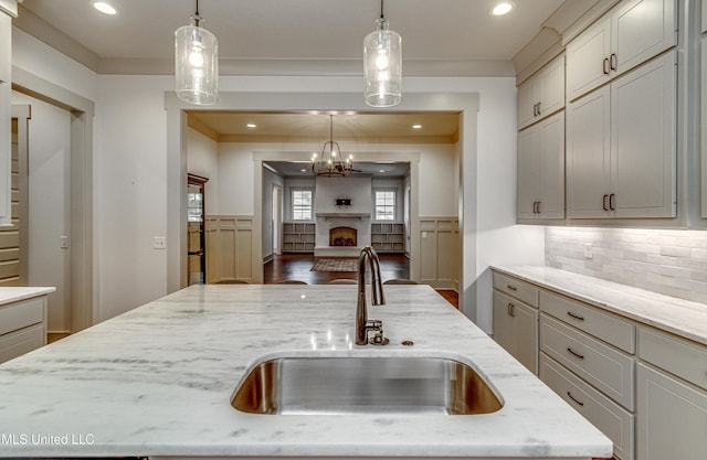 kitchen featuring light stone countertops, sink, pendant lighting, and an island with sink