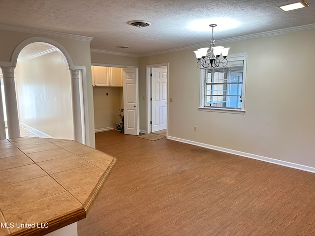 unfurnished dining area featuring a textured ceiling, hardwood / wood-style floors, ornate columns, crown molding, and a notable chandelier