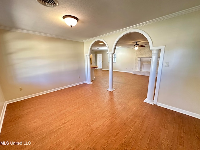 unfurnished room with ceiling fan, ornamental molding, a brick fireplace, and hardwood / wood-style floors