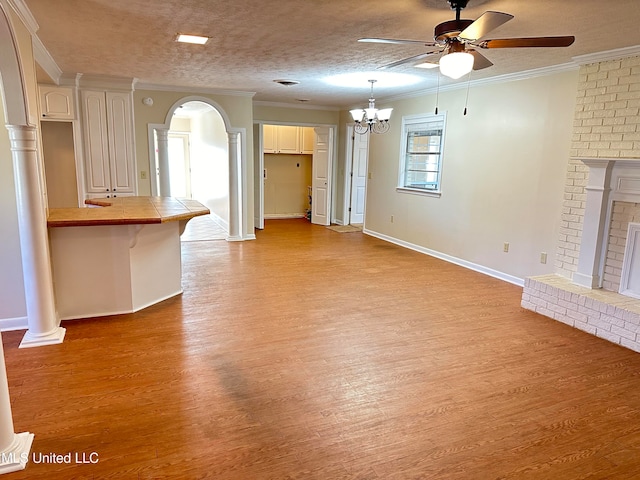 unfurnished living room featuring a textured ceiling, light hardwood / wood-style flooring, ceiling fan with notable chandelier, a fireplace, and crown molding