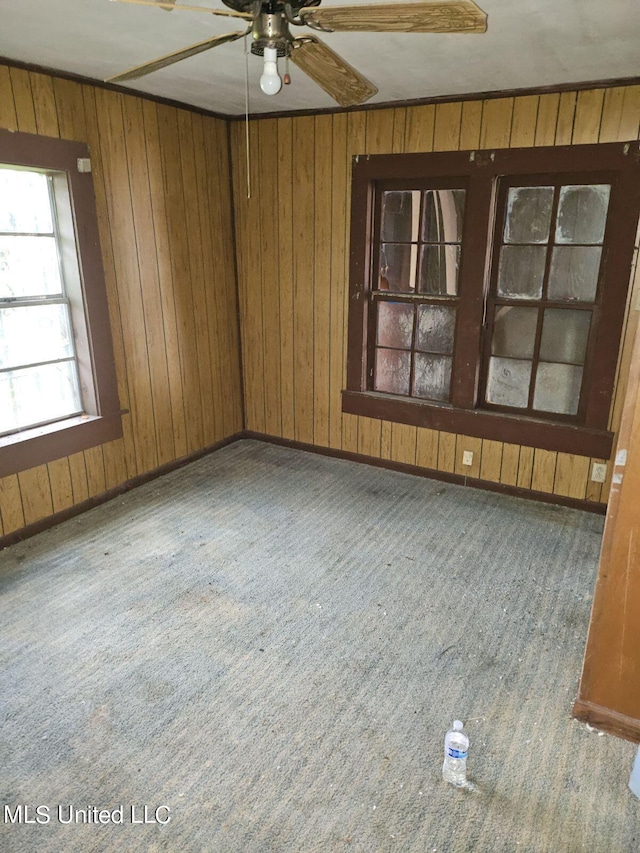 carpeted spare room featuring wood walls and ceiling fan