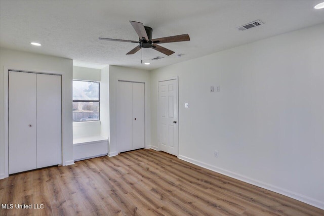 unfurnished bedroom with a textured ceiling, wood finished floors, two closets, and visible vents