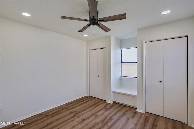 unfurnished bedroom with recessed lighting, wood finished floors, baseboards, and two closets