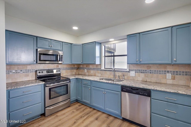 kitchen featuring appliances with stainless steel finishes, light wood-style floors, a sink, and blue cabinetry