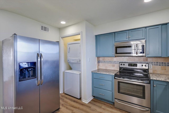 kitchen with appliances with stainless steel finishes, stacked washer / drying machine, visible vents, and blue cabinetry