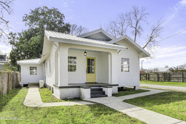 bungalow featuring metal roof, covered porch, fence, a front yard, and stucco siding