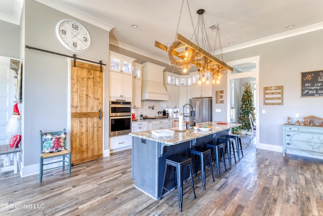 kitchen featuring light stone countertops, custom range hood, pendant lighting, a barn door, and a center island with sink