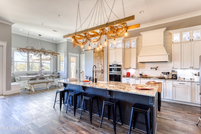 kitchen featuring crown molding, a center island with sink, stainless steel appliances, and custom exhaust hood