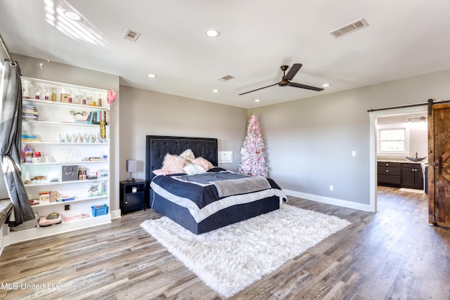 bedroom featuring hardwood / wood-style floors, a barn door, and ceiling fan