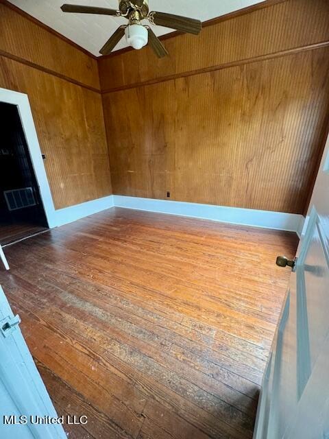 unfurnished room with hardwood / wood-style floors, wooden walls, and ceiling fan