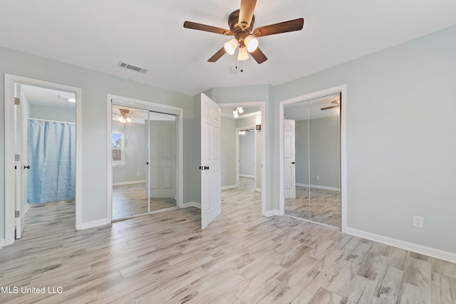 unfurnished bedroom with light hardwood / wood-style floors, ceiling fan, and two closets