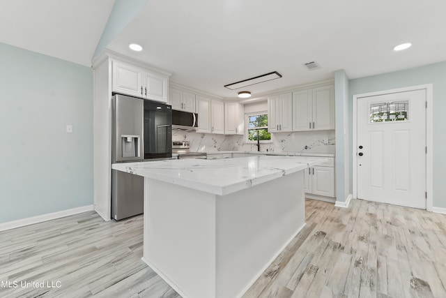 kitchen featuring white cabinetry, stainless steel appliances, a kitchen island, and light stone countertops