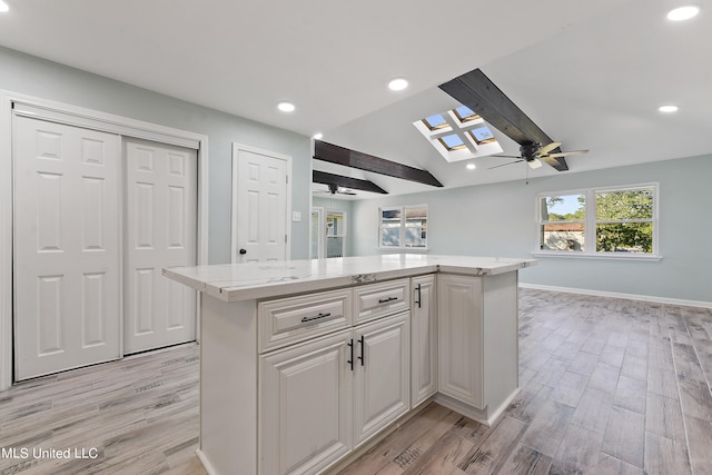 kitchen with lofted ceiling with skylight, a kitchen island, white cabinetry, and light hardwood / wood-style floors