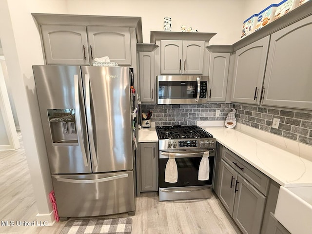 2290 Loisy Blvd, Hernando, MS 38632 - kitchen with stainless steel appliances, gray cabinetry, light wood finished floors, tasteful backsplash, and light stone counters