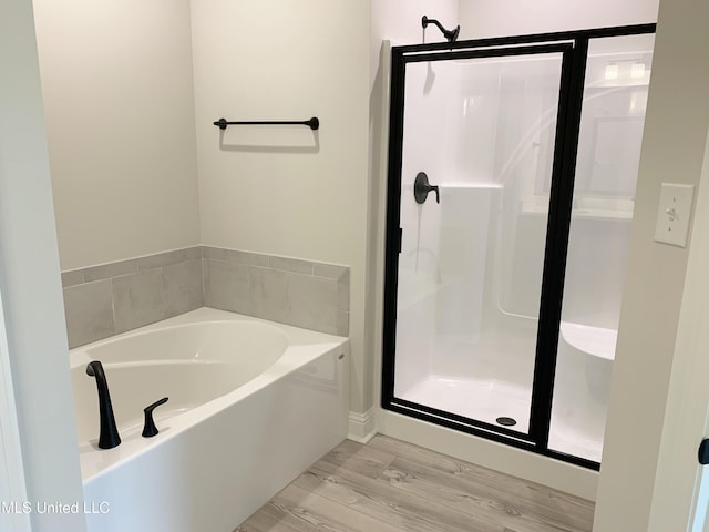 full bathroom with a stall shower, a bath, and wood finished floors