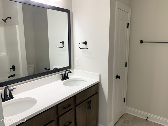 full bath featuring toilet, double vanity, a sink, and baseboards