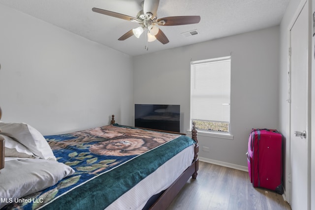 bedroom with a textured ceiling, wood-type flooring, and ceiling fan