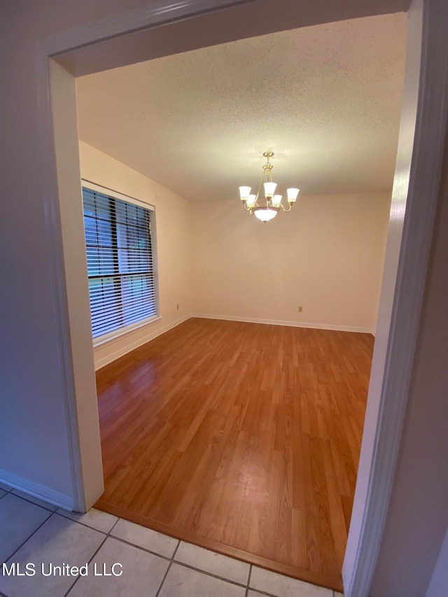 empty room featuring hardwood / wood-style flooring, a textured ceiling, and an inviting chandelier