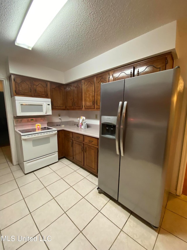 kitchen featuring a textured ceiling, light tile patterned floors, and white appliances