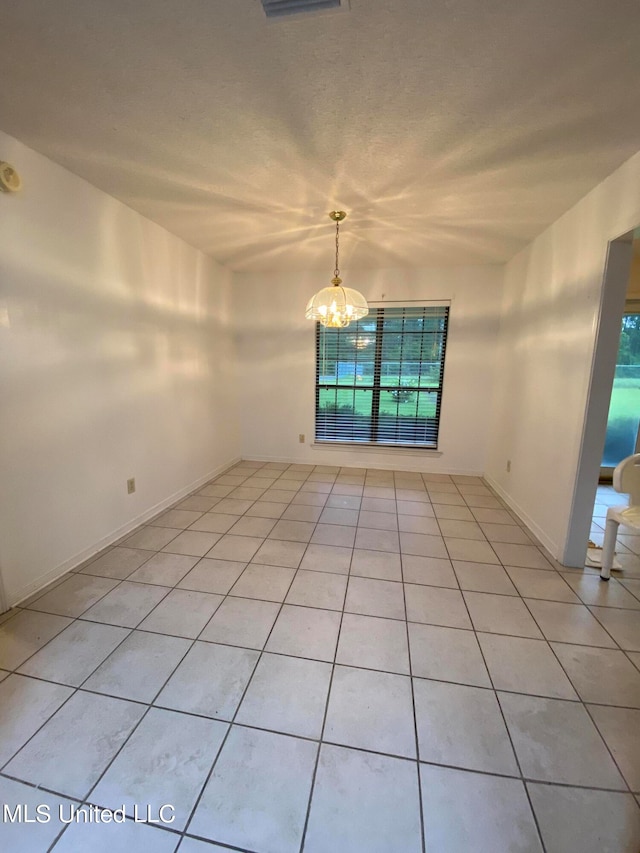 tiled spare room featuring a healthy amount of sunlight and a chandelier