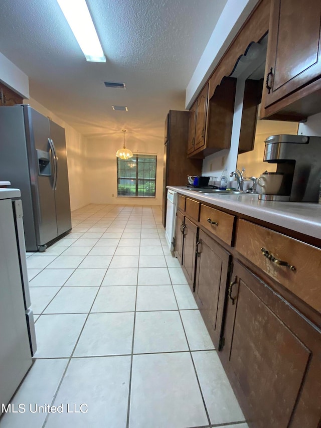 kitchen with light tile patterned flooring, a textured ceiling, stainless steel appliances, and sink