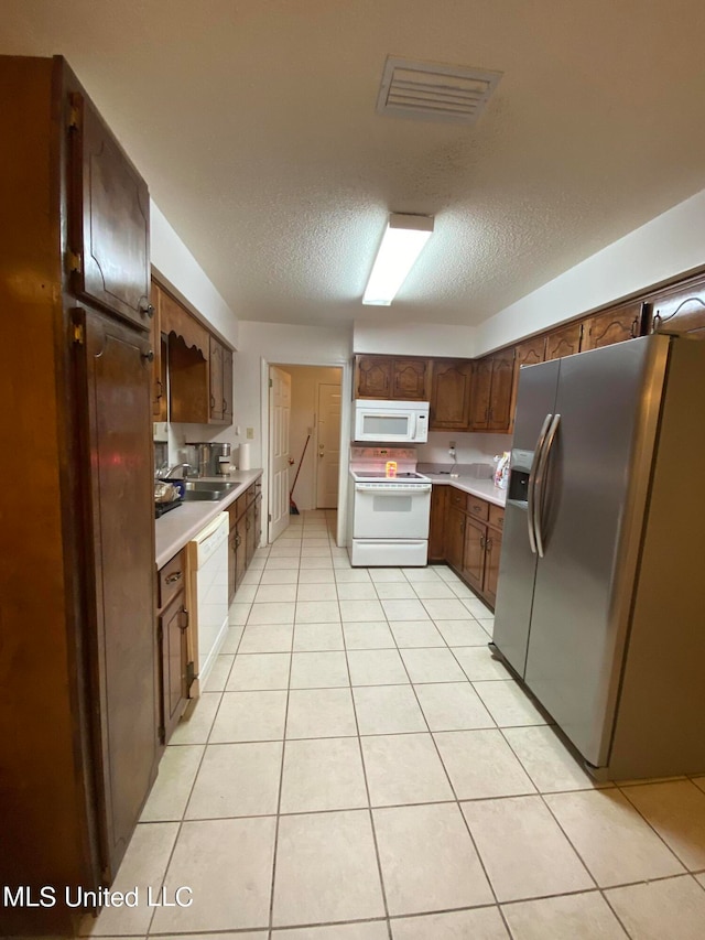 kitchen with a textured ceiling, light tile patterned flooring, sink, and white appliances