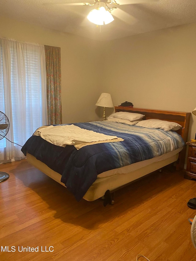 bedroom with ceiling fan, a textured ceiling, and light hardwood / wood-style flooring