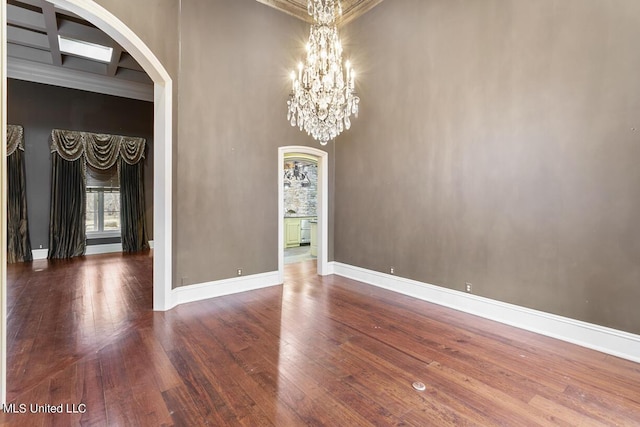 empty room with a towering ceiling, wood-type flooring, and a chandelier