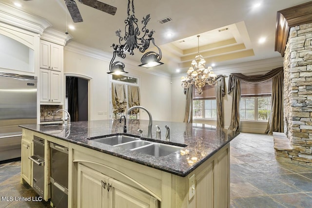 kitchen featuring built in refrigerator, sink, cream cabinets, and a center island with sink