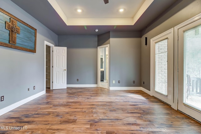 empty room featuring a wealth of natural light, a raised ceiling, baseboards, and wood finished floors