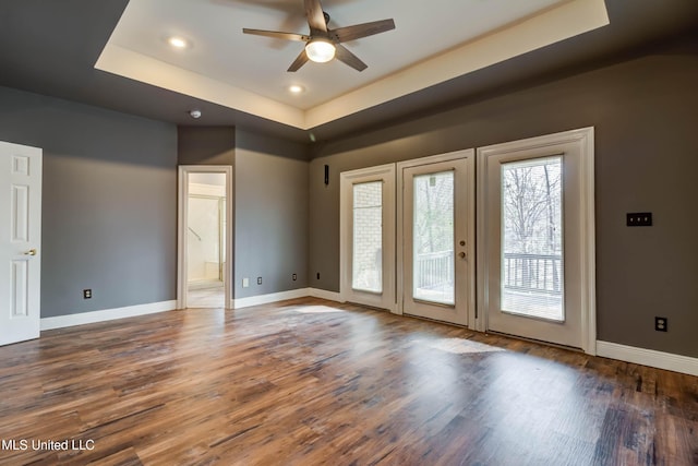 unfurnished room with ceiling fan, a tray ceiling, wood finished floors, and baseboards