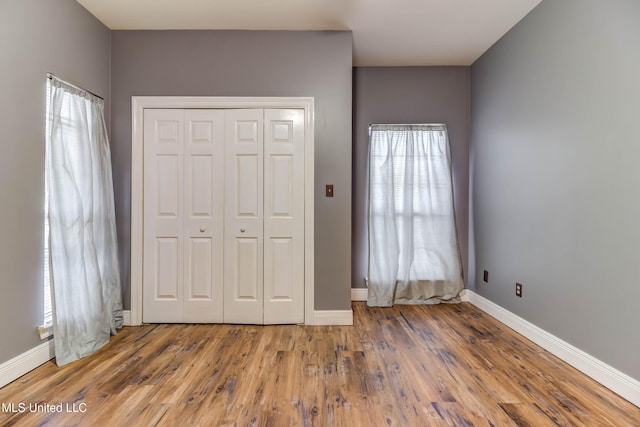 unfurnished bedroom featuring hardwood / wood-style flooring, multiple windows, and baseboards