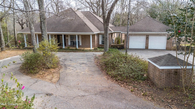 view of front of property featuring aphalt driveway, an attached garage, covered porch, brick siding, and roof with shingles