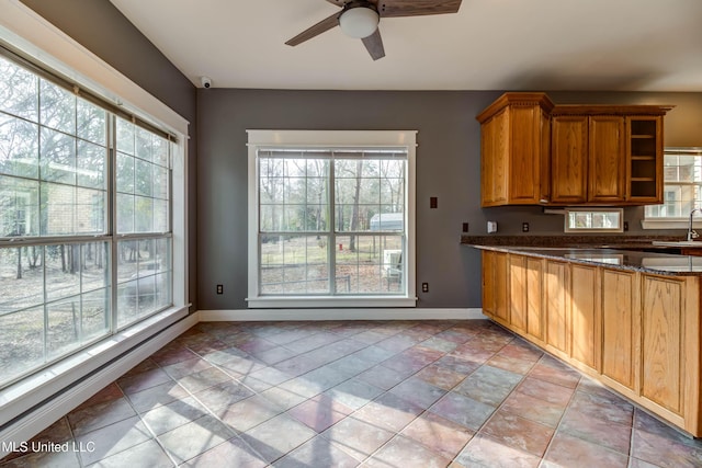 kitchen with a wealth of natural light, brown cabinets, a sink, and dark stone countertops