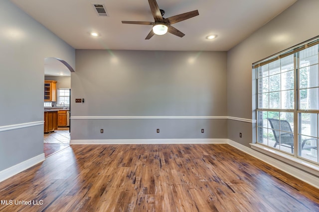 unfurnished room featuring arched walkways, wood finished floors, a ceiling fan, visible vents, and baseboards