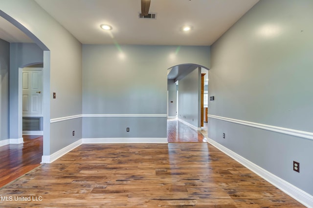 empty room featuring arched walkways, visible vents, and wood finished floors